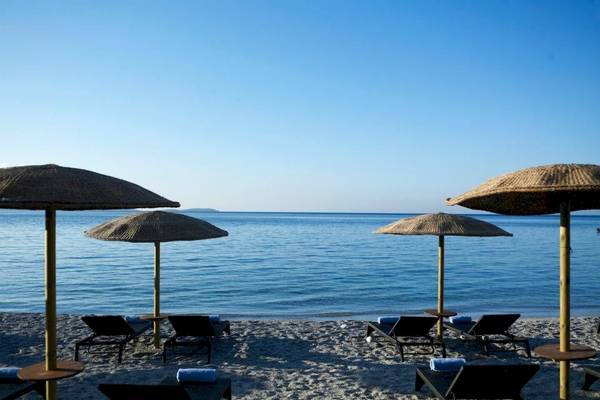 Strandszene des Proteas Blu Resorts mit Sonnenliegen und Strohschirmen am Meer.
