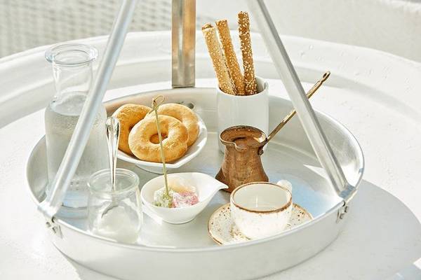Frühstücksplatte mit Gebäck, Getränken und Zubehör auf einem runden Tablett.
