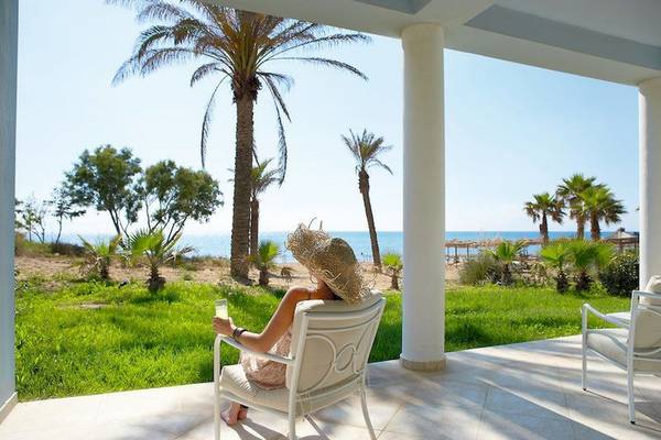 Frau sitzt auf Terrasse am Strand vor Palmen und genießt den Blick auf das Meer.