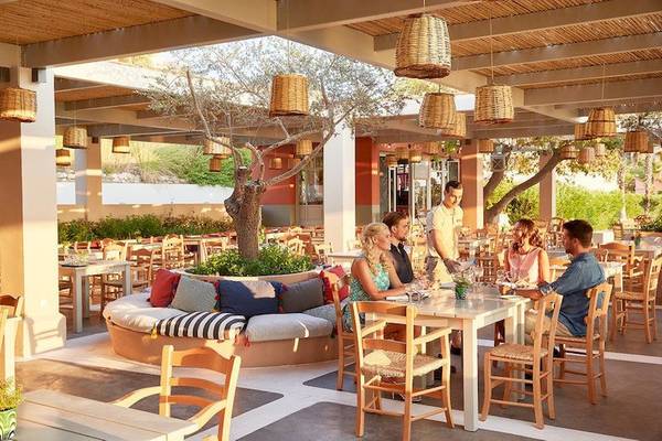 Gäste sitzen an Tischen in einem freien Restaurantbereich des Grecotel Olympia Oasis Aqua Park Hotels.