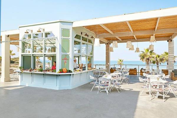 Außenbereich des Grecotel Olympia Oasis Aqua Park mit Terrasse, Tischen und Stühlen.