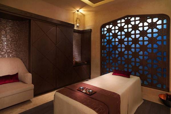 Spa-Behandlungsraum im Ritz Carlton Abu Dhabi Grand Canal mit Massageliege, Kissen und Holzschrank.