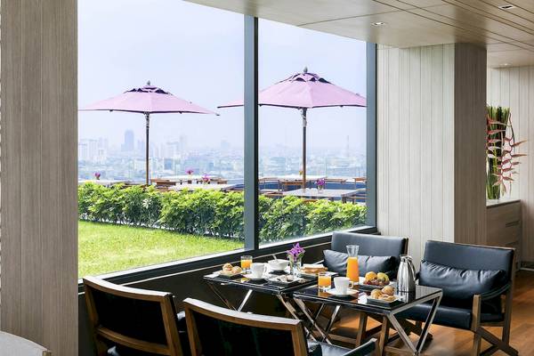 Frühstückstisch im Mercure Bangkok Siam mit Blick auf die Stadt und grüner Rasenfläche draußen.