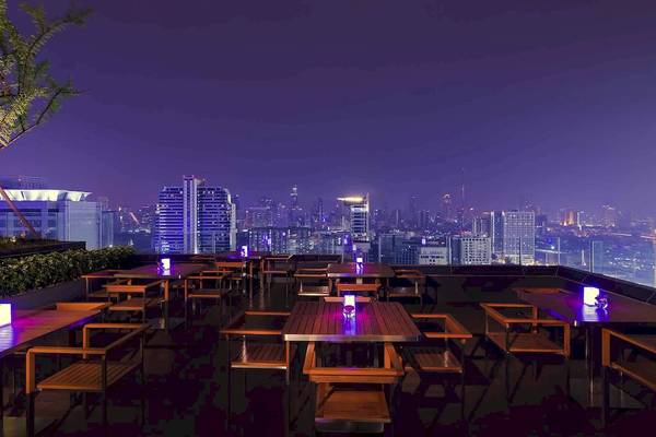 Nachtansicht der Dachterrasse des Mercure Bangkok Siam Hotels mit blau beleuchteten Tischen und Stühlen.