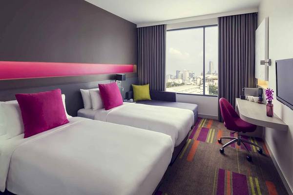 Innenansicht eines Doppelzimmers im Mercure Bangkok Siam Hotel mit zwei Betten, Sofa und Schreibtisch.