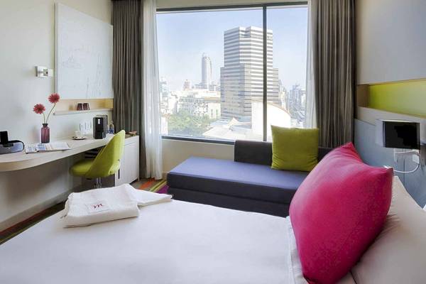 Ein Zimmer im Mercure Bangkok Siam Hotel mit Blick auf die Stadt, einem Bett, einem Schreibtisch und einem Fenster mit Ausblick.