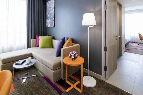 Innenansicht eines Hotelzimmers im Mercure Bangkok Siam mit einer gemütlichen Sitzecke, einem Tisch mit Blumen und einer Stehlampe.