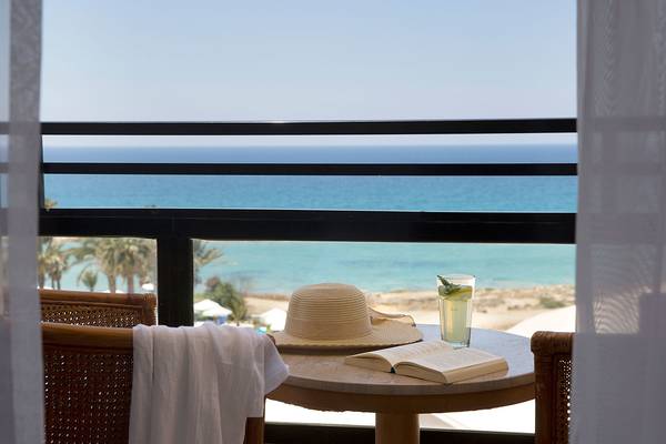 Aussicht auf das Meer vom Balkon des Venus Beach Hotels mit Tisch, Hut und Glas.