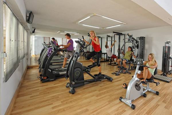 Fitnessraum im Aphrodite Beach Club mit mehreren Personen, die auf verschiedenen Geräten trainieren.