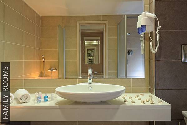 Badezimmer im Aphrodite Beach Club Familienzimmer mit Waschbecken, Spiegel und Handtüchern.