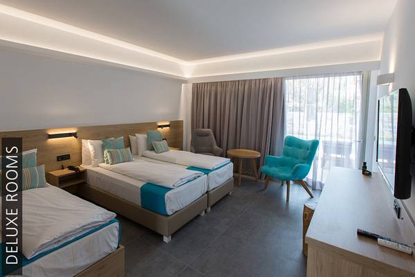 Deluxe Zimmer im Aphrodite Beach Club mit drei Betten, Möbeln und Fernseher.