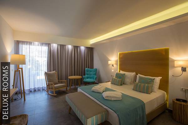 Ein Deluxe Zimmer im Aphrodite Beach Club mit einem großen Bett, Sesseln, Tisch und Lampen.