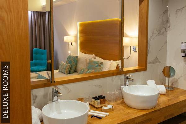 Das Badezimmer des Aphrodite Beach Club Deluxe Zimmers mit zwei Waschbecken und einem Spiegel.
