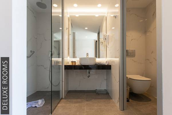 Badezimmer im Aphrodite Beach Club Deluxe Room mit Glasdusche, Waschbecken und Toilette.