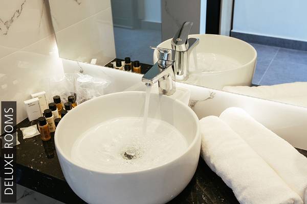 Ein Deluxe Badezimmer im Aphrodite Beach Club mit einem Waschbecken, das Wasser fließt, und Handtüchern.
