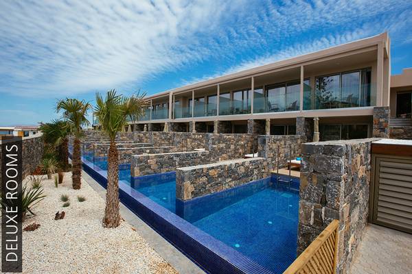 Außenbereich des Aphrodite Beach Club Hotels mit mehreren Schwimmbecken, Steinmauern und Palmen