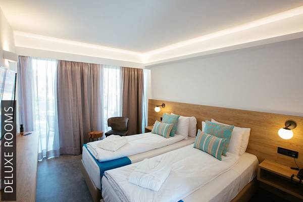 Zwei Betten in einem Deluxe-Zimmer des Aphrodite Beach Club mit modernen Möbeln und blauen Kissen.