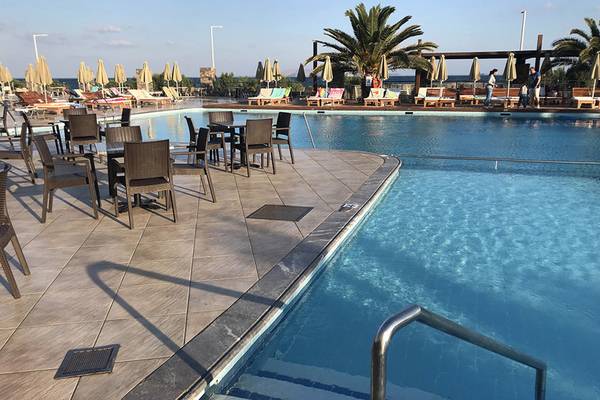 Poolbereich des Aphrodite Beach Clubs mit Sonnenliegen, Tischen und Stühlen.