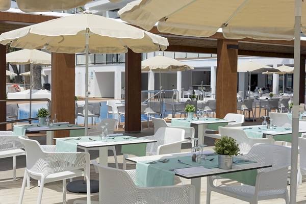 Außenbereich des HSM Linda Playa Hotels mit gepolsterten Stühlen und Tischen unter Sonnenschirmen.