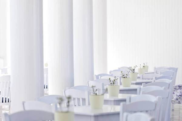 Innenbereich des Mrs Chryssana Beach Hotels mit weißen Tischen und Stühlen und Pflanzen in Töpfen.