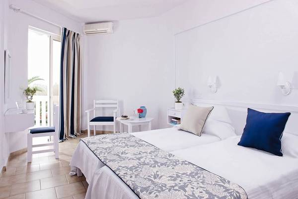Schlafzimmer im Mrs Chryssana Beach Hotel mit zwei Betten, Kissen, Nachttischen und einem offenen Fenster.