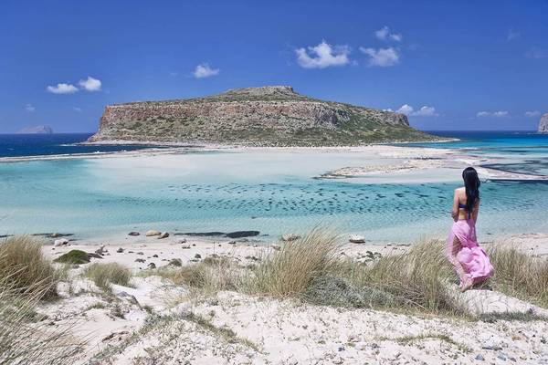 Frau in einem rosa Kleid am Mrs Chryssana Beach mit Blick auf eine Insel.