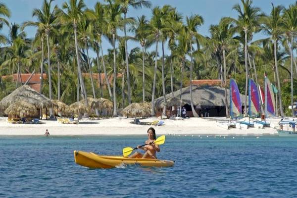 Frau im Kajak am Strand des Dreams Flora Resort & Spa mit Palmen und Segelbooten im Hintergrund.