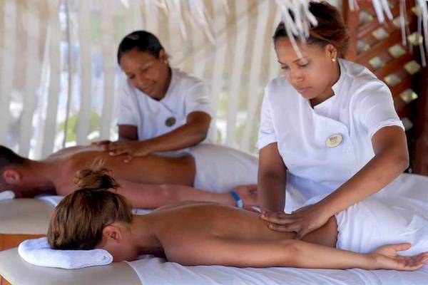 Massagebehandlung im Dreams Flora Resort & Spa mit zwei Frauen, die Rückenmassagen an zwei Männern durchführen.
