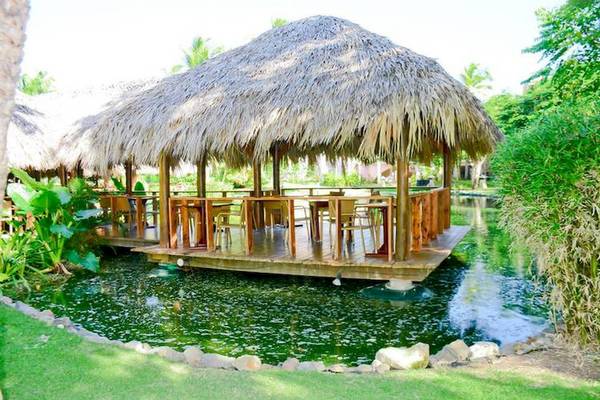 Restaurant im Dreams Flora Resort & Spa mit hügelgedeckter Terrasse über einem Teich.