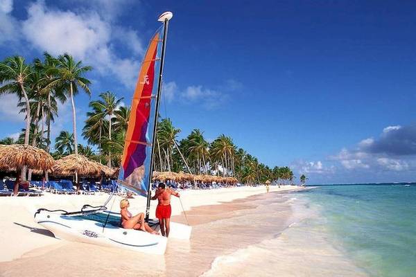 Ein Segelboot am Strand des Dreams Flora Resort & Spa mit zwei Personen und Palmen im Hintergrund.