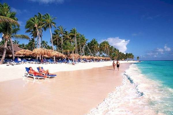 Strand mit weißen Palmen, Sonnenliegen und zwei Personen, die sich entspannen, und zwei Personen, die am Strand spazieren.