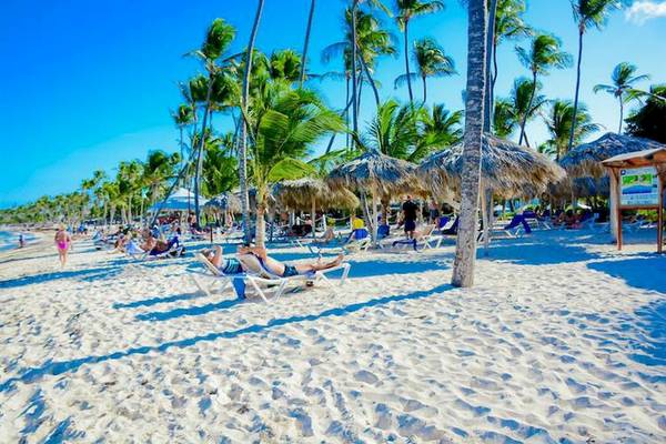 Strand mit vielen Palmen, Liegen und Sonnenschirmen, mehrere Menschen entspannen.
