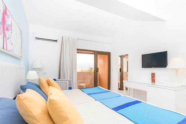Schlafzimmer im Be Live Experience Las Morlas Hotel mit zwei Betten, blauen und gelben Kissen, Fernseher und Fenstern.