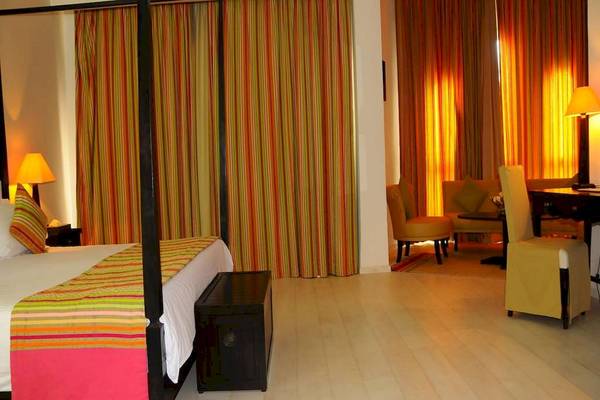 Schlafzimmer im Golden Tulip Taj Sultan Hotel mit viersäuligem Bett, bunten Vorhängen und Wohnzimmermöbeln.