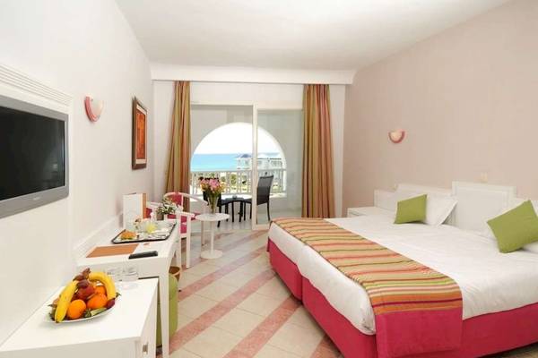 Innenansicht des Golden Tulip Taj Sultan Hotels mit einem Doppelbett, Früchten und einem Ausblick auf das Meer.