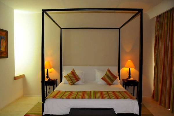 Schlafzimmer im Golden Tulip Taj Sultan Hotel mit vierposterbett, leuchtenden Lampen und gestreiften Kissen.