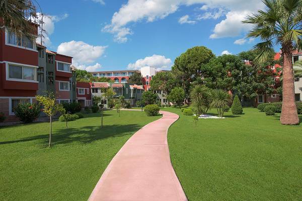Außenbereich des Megasaray Club Belek Hotels mit Rasen und Gehweg.