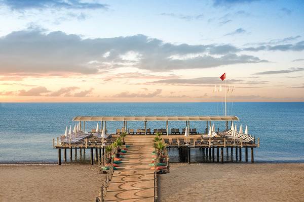 Abendaufnahme des Megasaray Club Belek mit einer Holzpier und Sonnenliegen am Meer