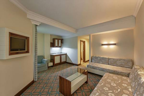 Innenansicht der Suite im Megasaray Club Belek Hotel mit Wohnzimmer, Fernseher und Küchenbereich.