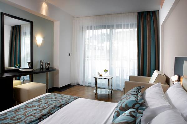 Innenansicht eines eleganten Hotelzimmers mit großem Bett, Schreibtisch und Fenstern.