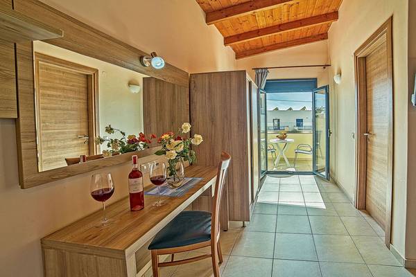 Innenansicht eines Zimmers im Blue Aegean Hotel & Suites mit Tisch, Weinflasche und zwei Gläsern, einem Spiegel und einem offenen Balkon.