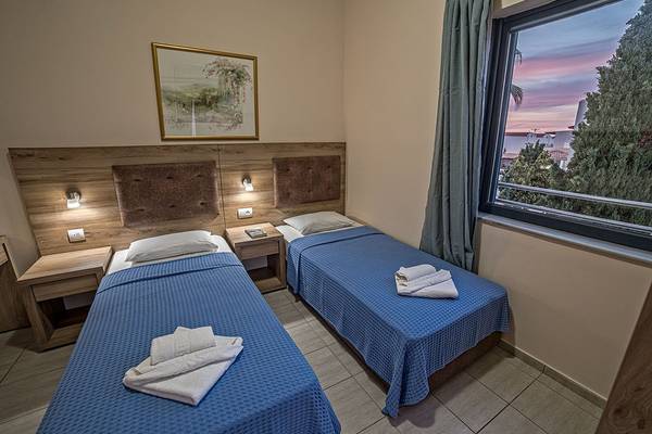 Zwei Betten im Hotelzimmer des Blue Aegean Hotel & Suites mit Ausblick auf die Stadt.