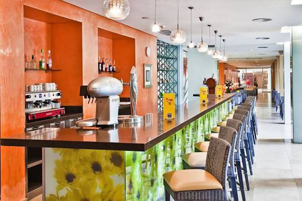 Rezeption des Barcelo Margaritas Hotels mit Bar und Stühlen, orangefarbene Wände und gelbe Blumen auf der Theke.