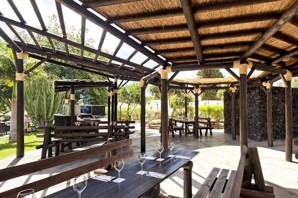 Gartenrestaurant im Barcelo Margaritas Hotel mit hölzernen Tischen und Bänken unter einem Strohdach.