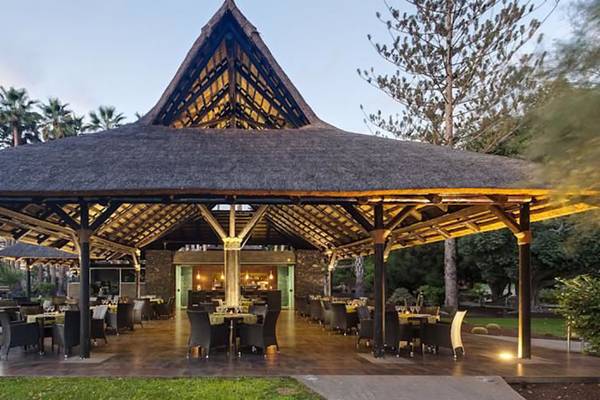 Außenbereich des Restaurants Barcelo Margaritas mit einem großen Strohdach und runden Tischen.