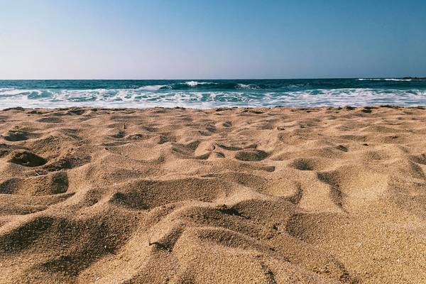 Strand mit feinem Sand und dem Meer im Hintergrund, wo Wellen sanft an die Küste stoßen.