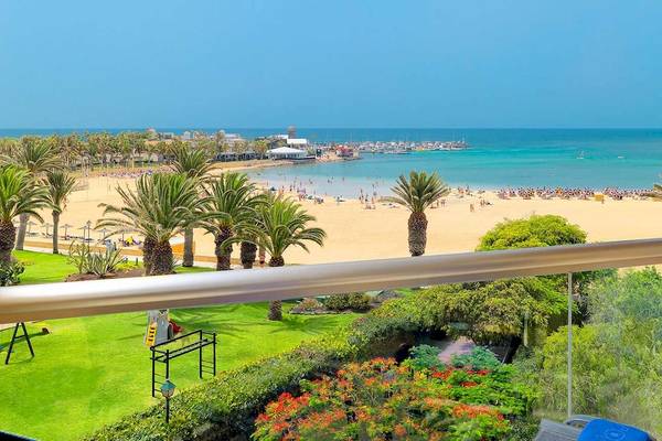 Aussicht vom Balkon des Barcelo Fuerteventura Mar auf einen breiten Sandstrand, blaues Meer und grüne Palmen.