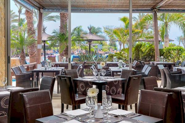 Innenansicht des Restaurants im Barcelo Fuerteventura Mar Hotel mit Tisch, Stühlen und Palmen im Hintergrund.