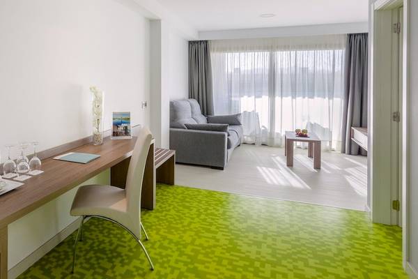 Innenansicht eines Zimmers im Barcelo Fuerteventura Mar Hotel mit Schreibtisch, Stuhl, Couch und Fenstern.