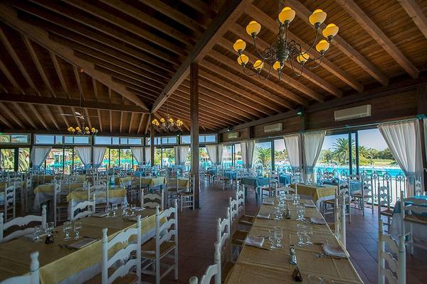 Foto des Innenbereichs des Club Hotel Marina Beach, zeigt ein geräumiges Restaurant mit Tischen und Stühlen, großen Fenstern und einer Aussicht auf den Pool.